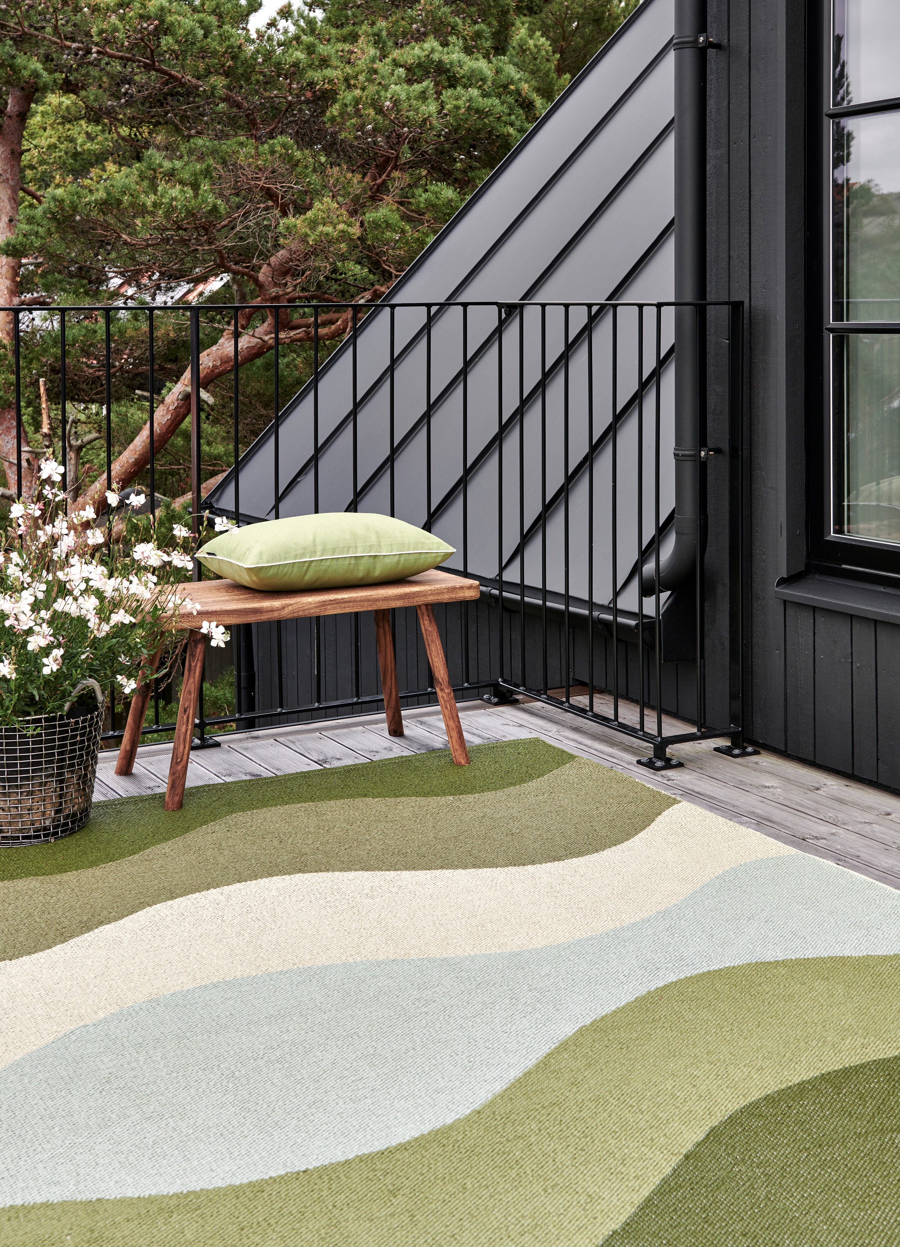 a green hue waved rug from Pappelina on a balcony featureing greenerie and a dark wooden exterior
